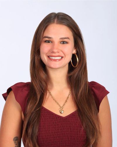 Smiling woman with long brown hair wearing a maroon dress and gold jewelry.