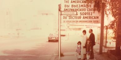 A family stands near a multilingual checkpoint sign at an entrance.