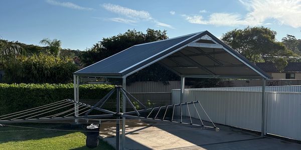 Backyard with a rotary clothesline and a metal carport under clear blue sky.