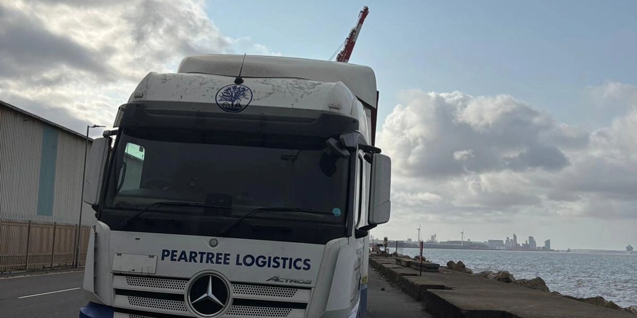 A Peartree Logistics truck parked near a waterfront under a cloudy sky.