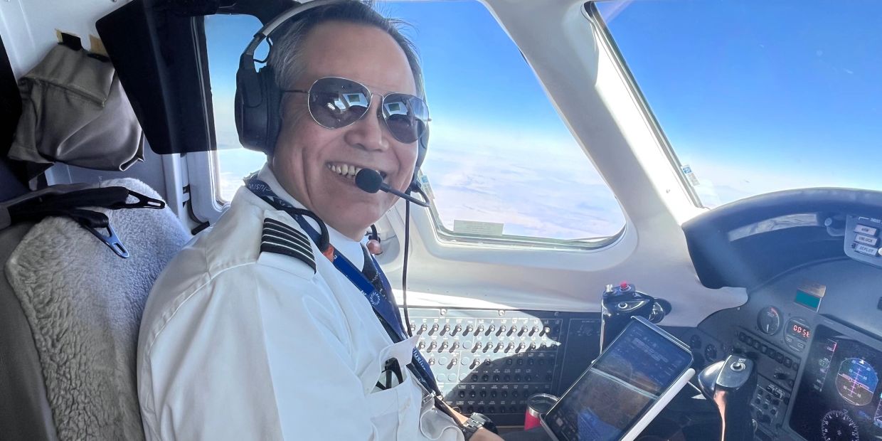 Smiling pilot in cockpit wearing sunglasses and headset.
