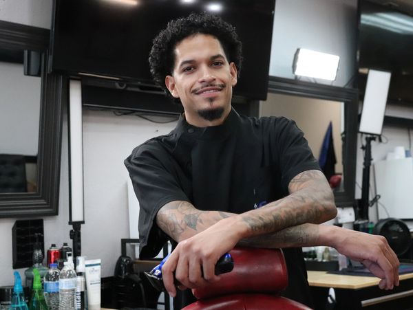 Smiling barber leaning on a chair with clippers in hand inside Crispcutz barbershop.