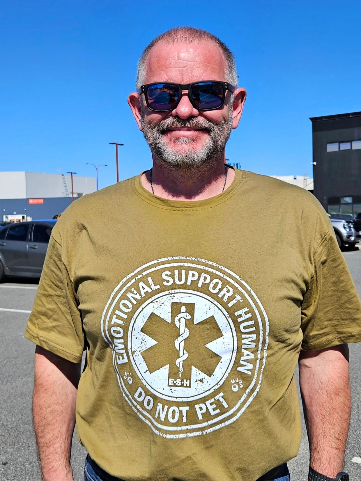 Smiling man wearing sunglasses and a green t-shirt with text.