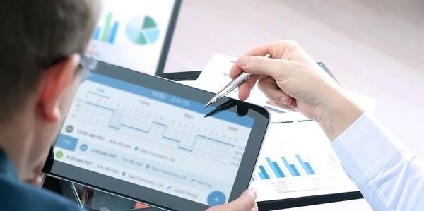 Two people analyzing data charts on a tablet and printed documents.