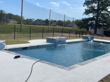 A rectangular swimming pool in a backyard under a clear sky.