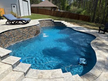 Backyard swimming pool with steps and stone wall.