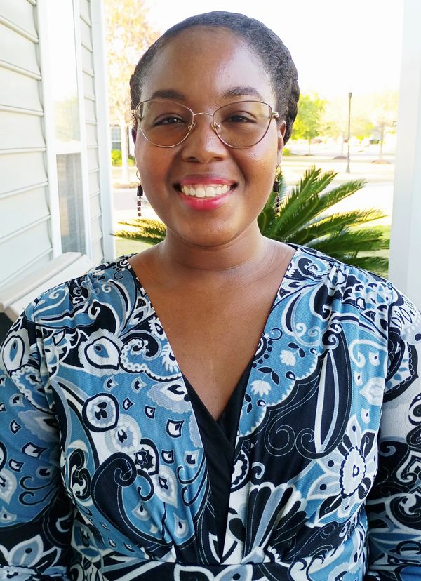 Smiling woman with glasses in patterned blue dress outdoors.