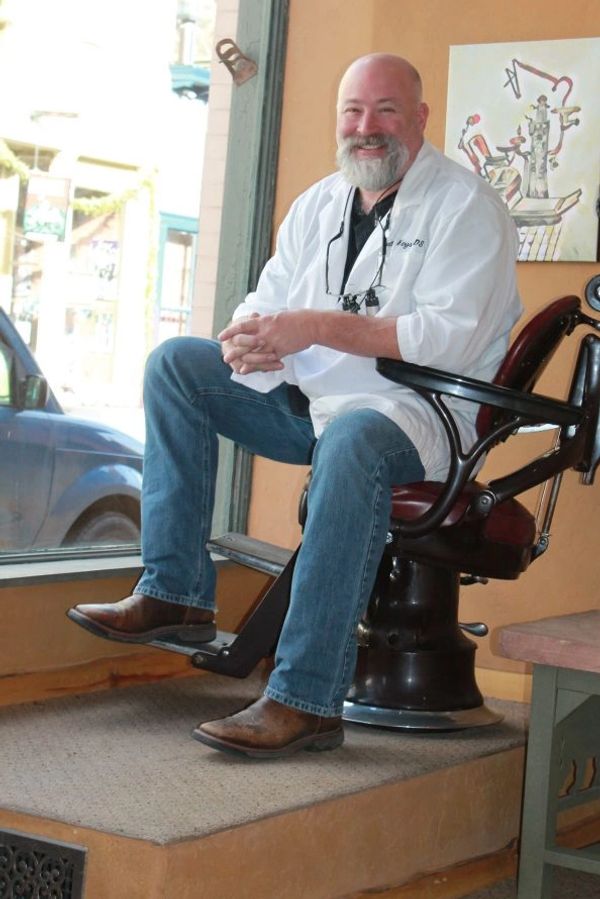 Smiling barber sitting on a vintage barber chair inside a shop.