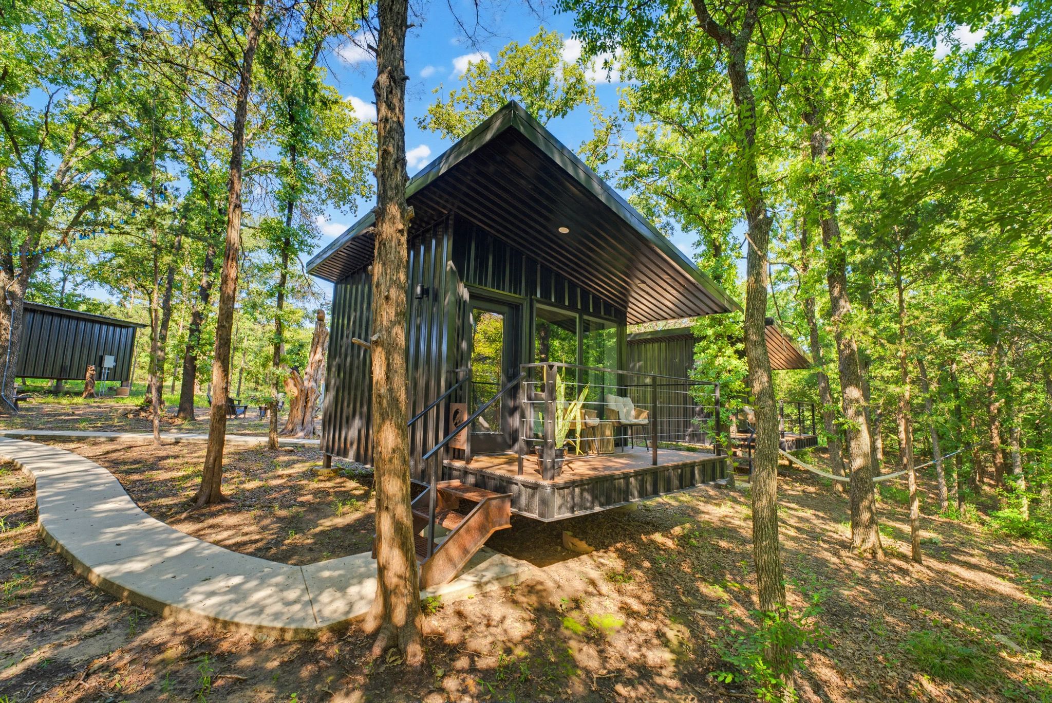 Modern black cabin in a green forest with a curved concrete path.