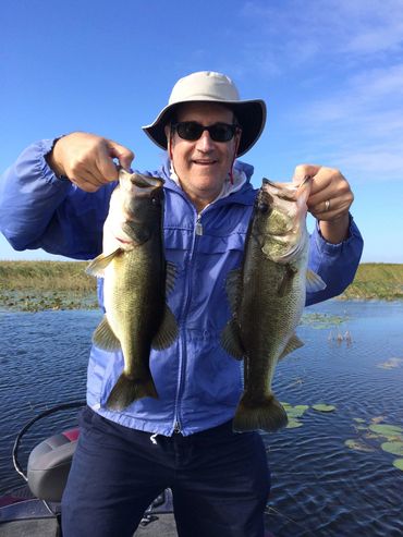 Man in blue jacket holding two large fish.