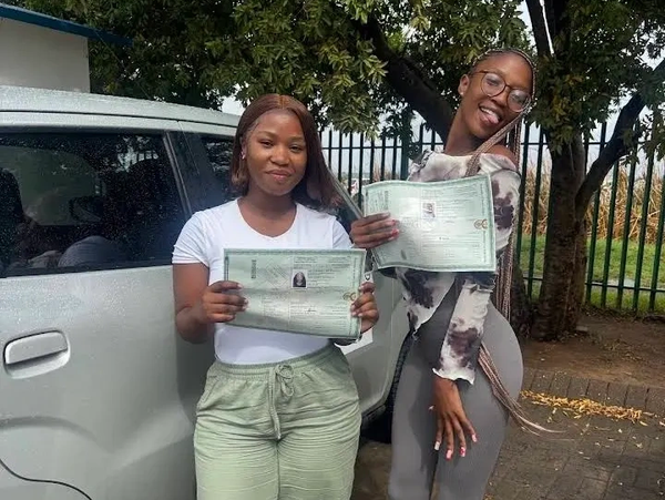 Two women proudly holding certificates outdoors.