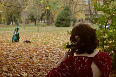 Woman playing violin in a park during autumn.