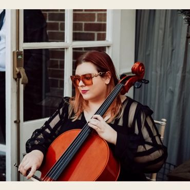 Woman playing cello with striped sheer sleeves and sunglasses.