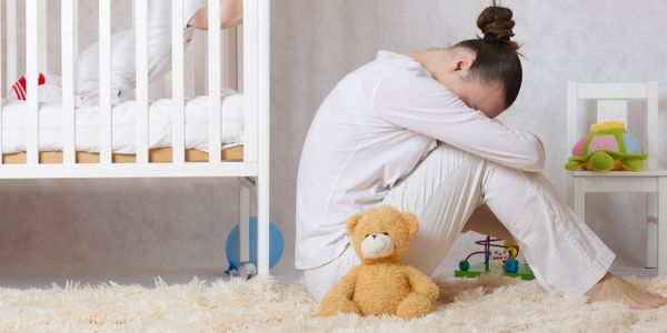 Woman sitting with her head down while her child looks out from its crib