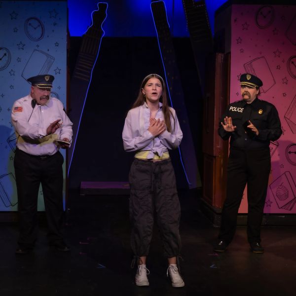 A young woman expresses emotion between two policemen on stage.