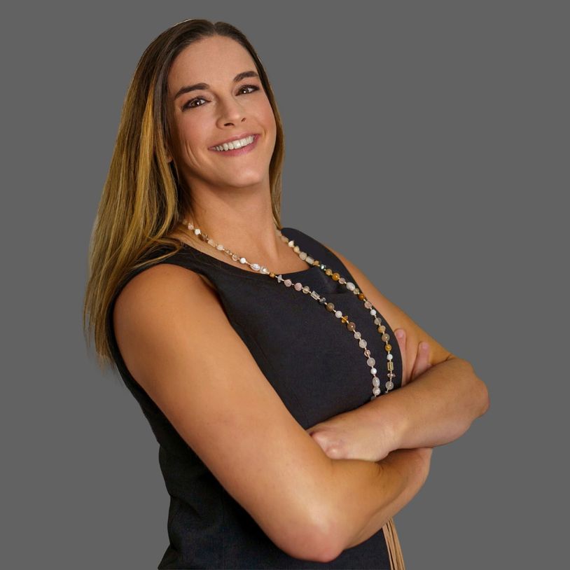 Confident woman with arms crossed, smiling against a grey backdrop.