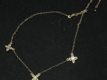 Delicate gold necklace with three flower-shaped pendants on a black background.