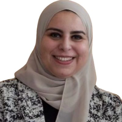 Smiling woman wearing a beige hijab and patterned jacket.