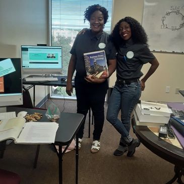 Two women smiling in an office holding a book on business technology.