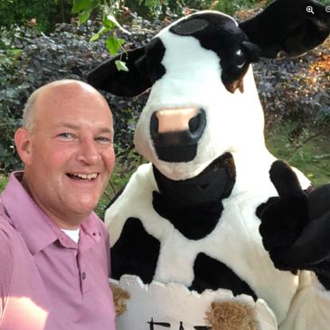 Man smiling next to person in cow costume giving thumbs up.