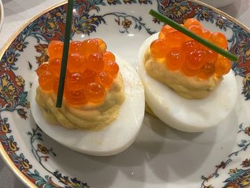 Deviled eggs topped with orange fish roe and chive garnish on a decorative plate.
