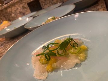 Delicate dish with thinly sliced fish, garnished with green onions and yellow sauce on a blue plate.