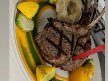Grilled rack of lamb with vegetables and onion rings on a white plate.