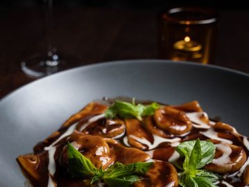 Gourmet ravioli with rich brown sauce and fresh basil garnish.