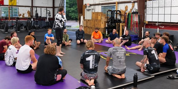 Group sitting on mats listening to a coach in a gym.