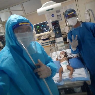 Healthcare workers in PPE attending to a patient in an ICU.