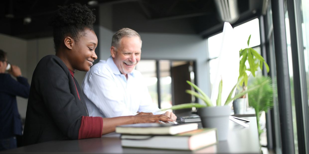 Two colleagues collaborate happily at a desk with books and plants.