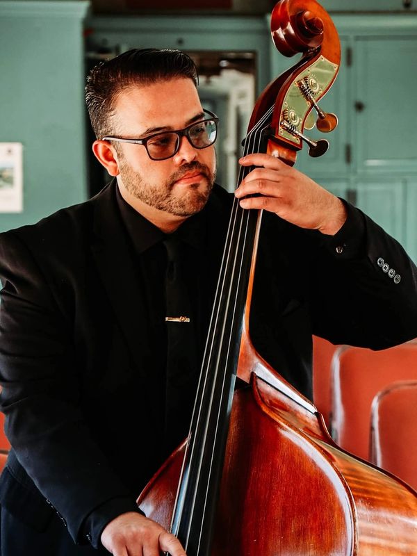 Man in black suit playing a double bass indoors.