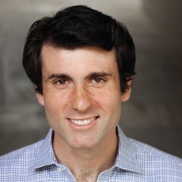 Smiling man with dark hair wearing a checkered shirt.
