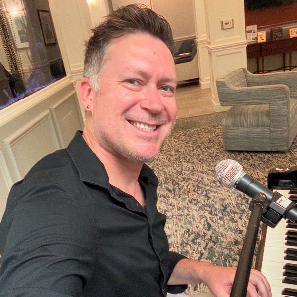 Man smiling while playing piano with microphone nearby indoors.