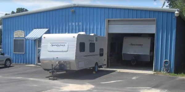 Two Sportsmen travel trailers near a blue metal building with a large garage door.
