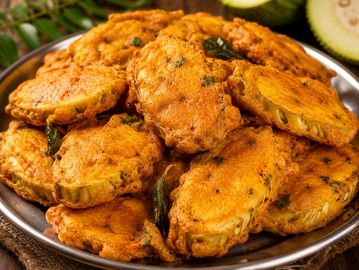 A plate of golden, crispy fried vegetable fritters garnished with curry leaves.