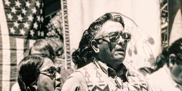 Historical black and white photo of Native American individuals with an American flag.