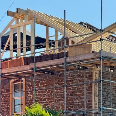House under construction with scaffolding and new roof framing.