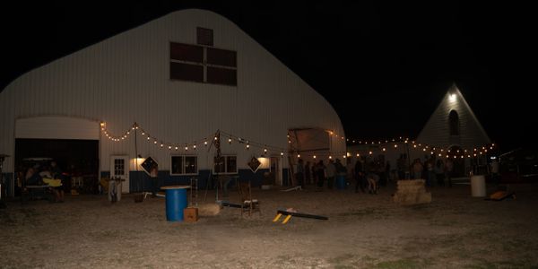 Nighttime outdoor gathering with string lights at a barn and nearby building.