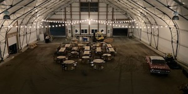Large indoor space with round tables, chairs, and string lights.