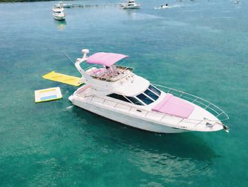 A white yacht with pink accents floating on clear blue water.