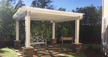 White pergola covering a stone and grass patio in the backyard