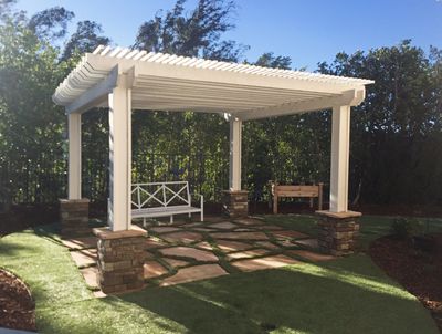 White pergola over a stone and grass patio