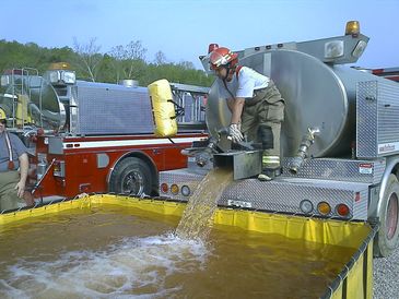Firefighter filling a portable water tank from a fire truck.