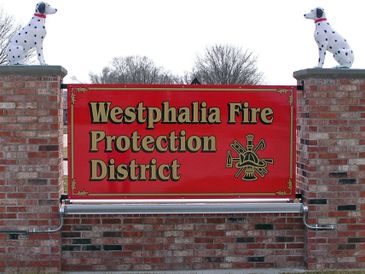 Sign for Westphalia Fire Protection District with Dalmatian statues on brick pillars.