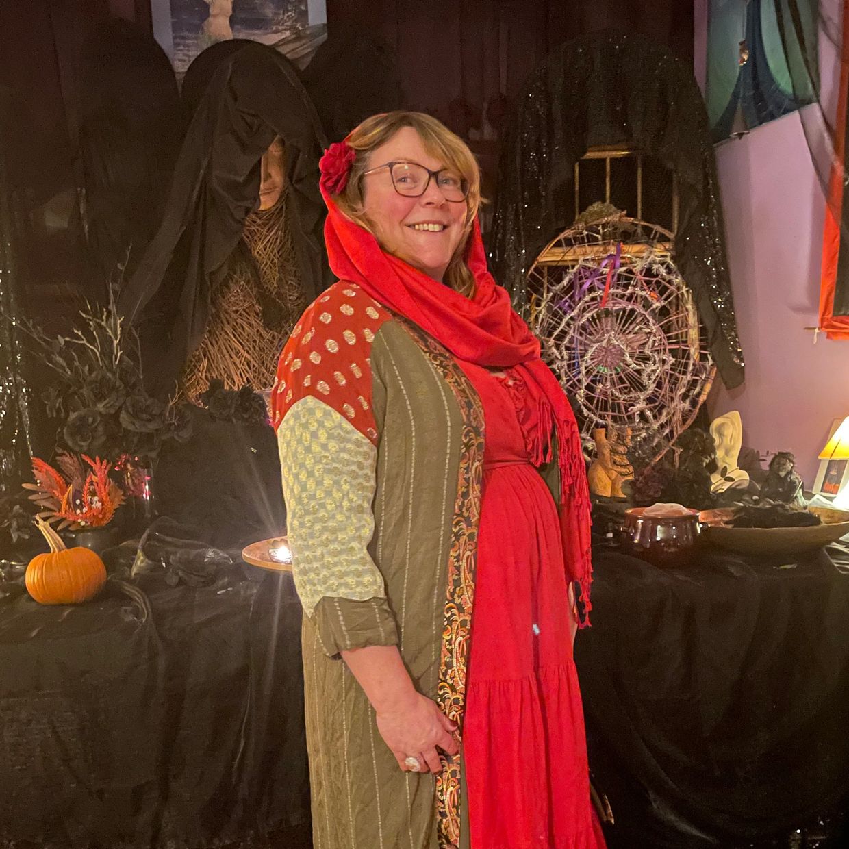 Smiling woman in a colorful dress and red scarf at a decorated indoor setting.