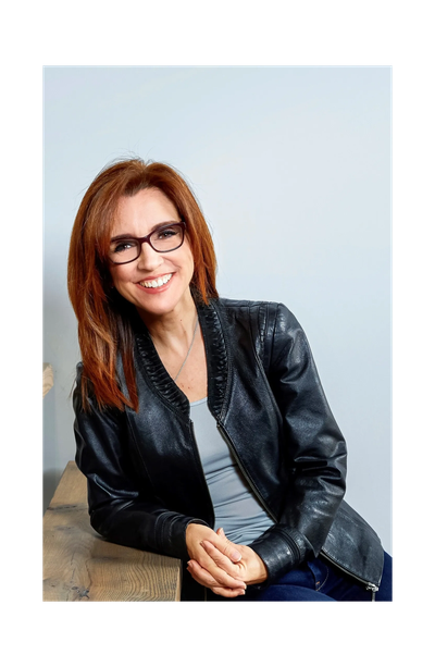 Smiling woman with red hair and glasses in a black leather jacket.