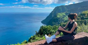 A woman sitting and admiring a scenic ocean view from a hillside.