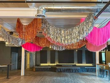 Colorful metallic and fringe decorations hang from a spacious room ceiling.