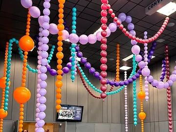 Colorful balloon chains hanging from the ceiling in a convention center.